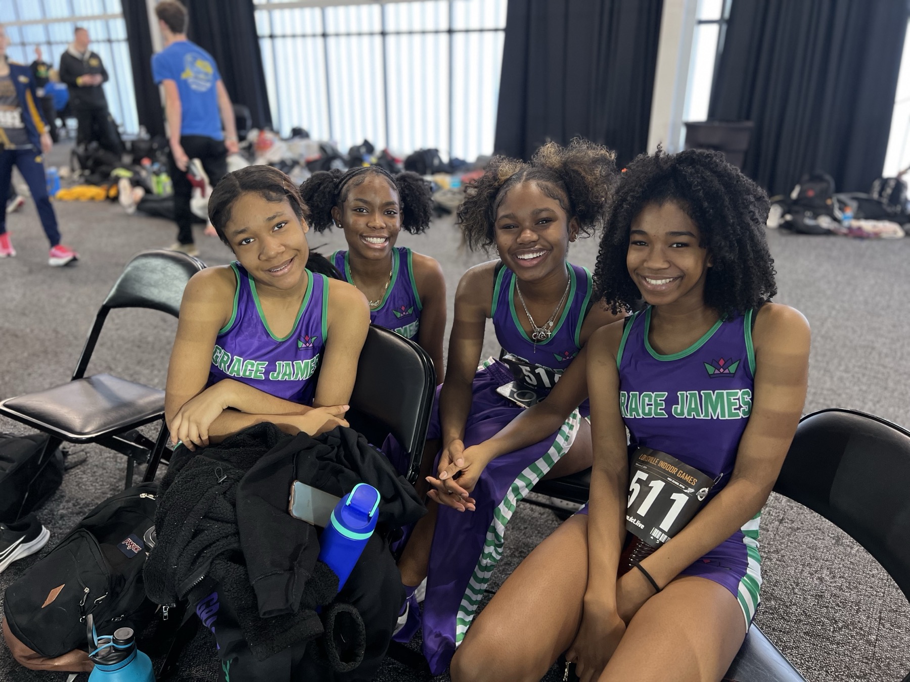 Four young track athletes in Grace James uniforms smiling together at the Louisville Indoor Games