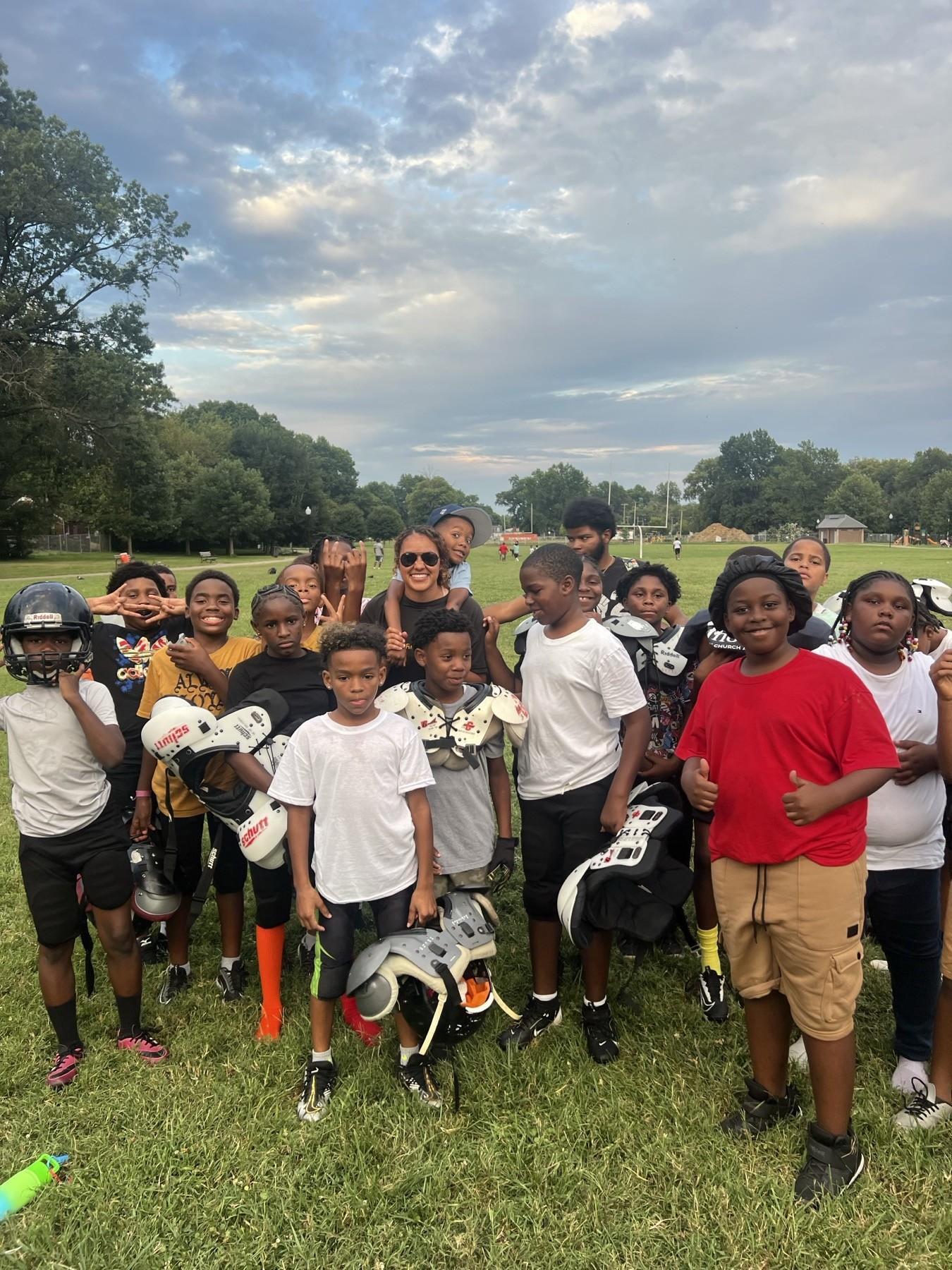 A youth football team in pads standing with a Huddle coach at a Louisville park