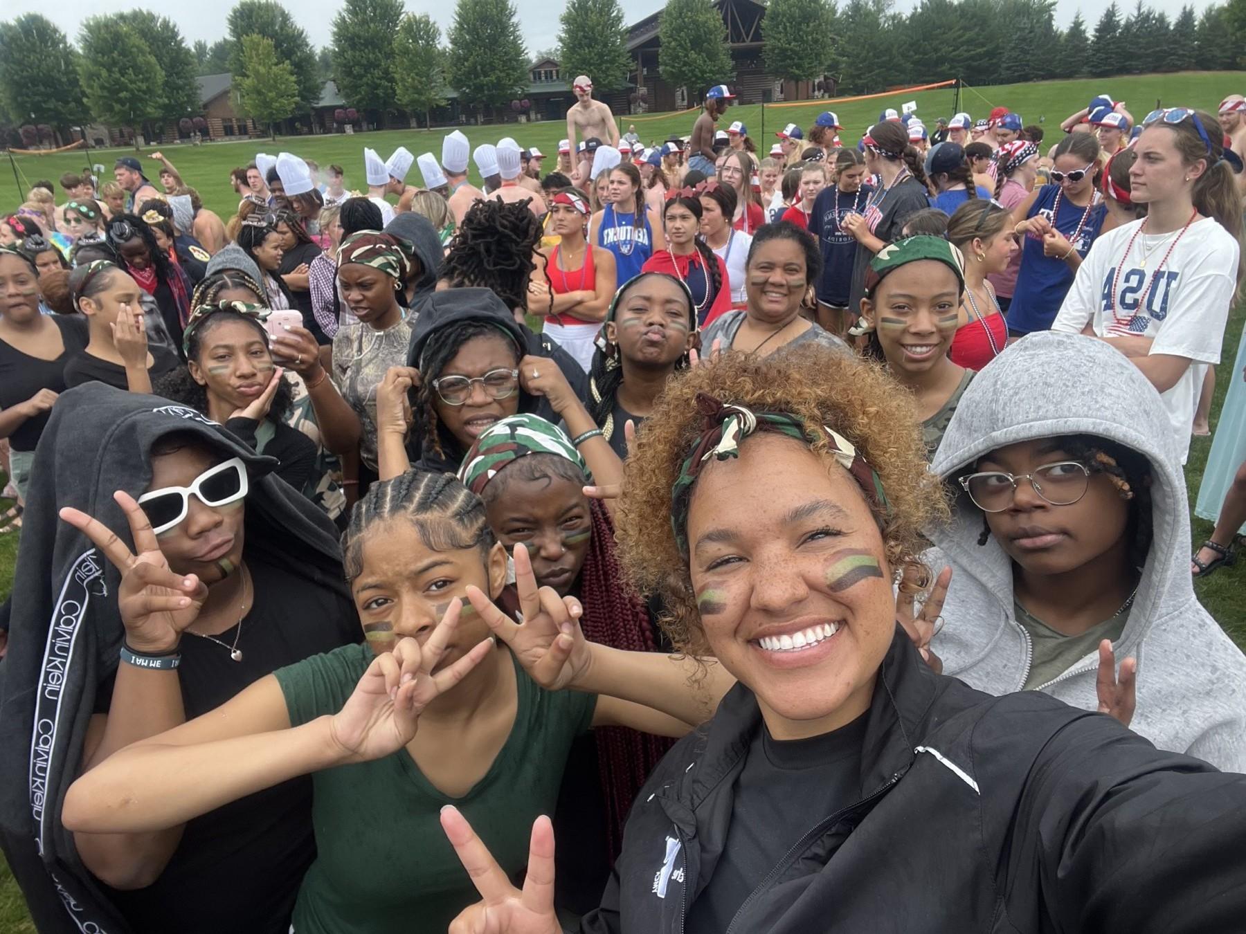 Huddle campers and staff wearing face paint and camo bandanas in a crowded camp field-day group selfie
