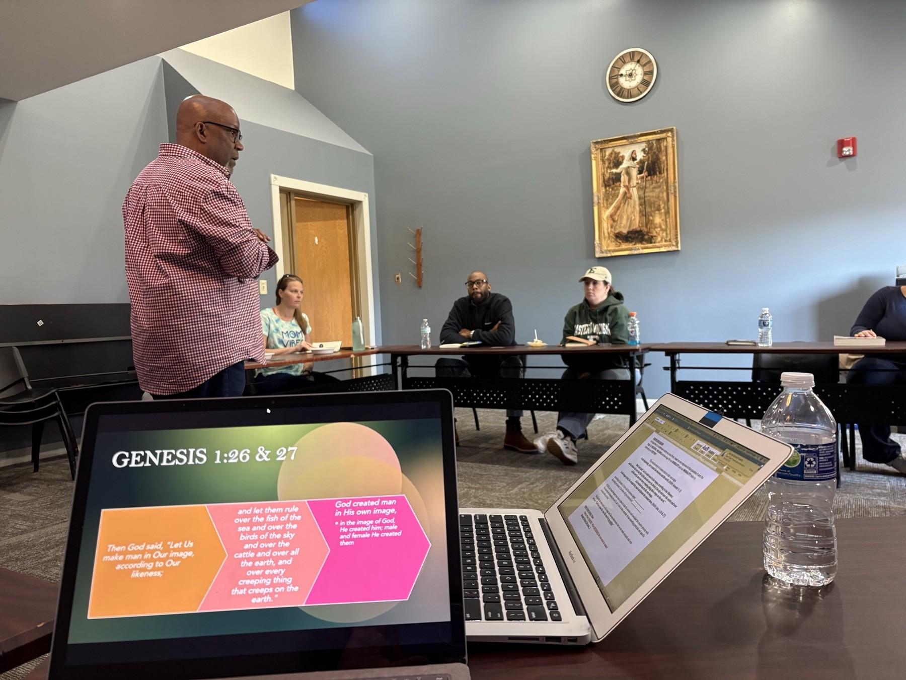 A Purpose Playbook facilitator presenting Genesis scripture slides to adults seated at tables during a live teaching session